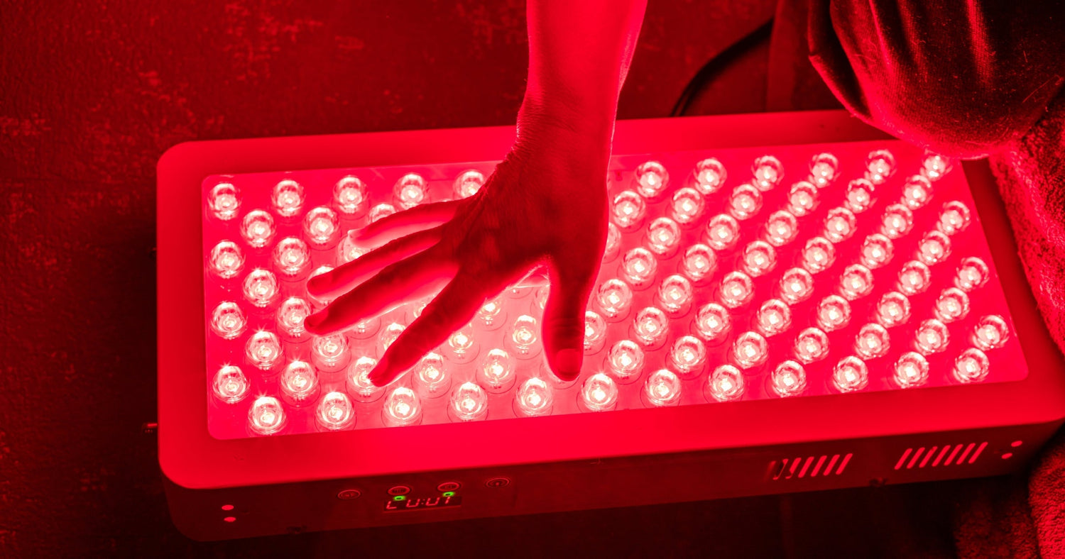 Hand over red LED light therapy panel, glowing in a dark room, skin treatment device