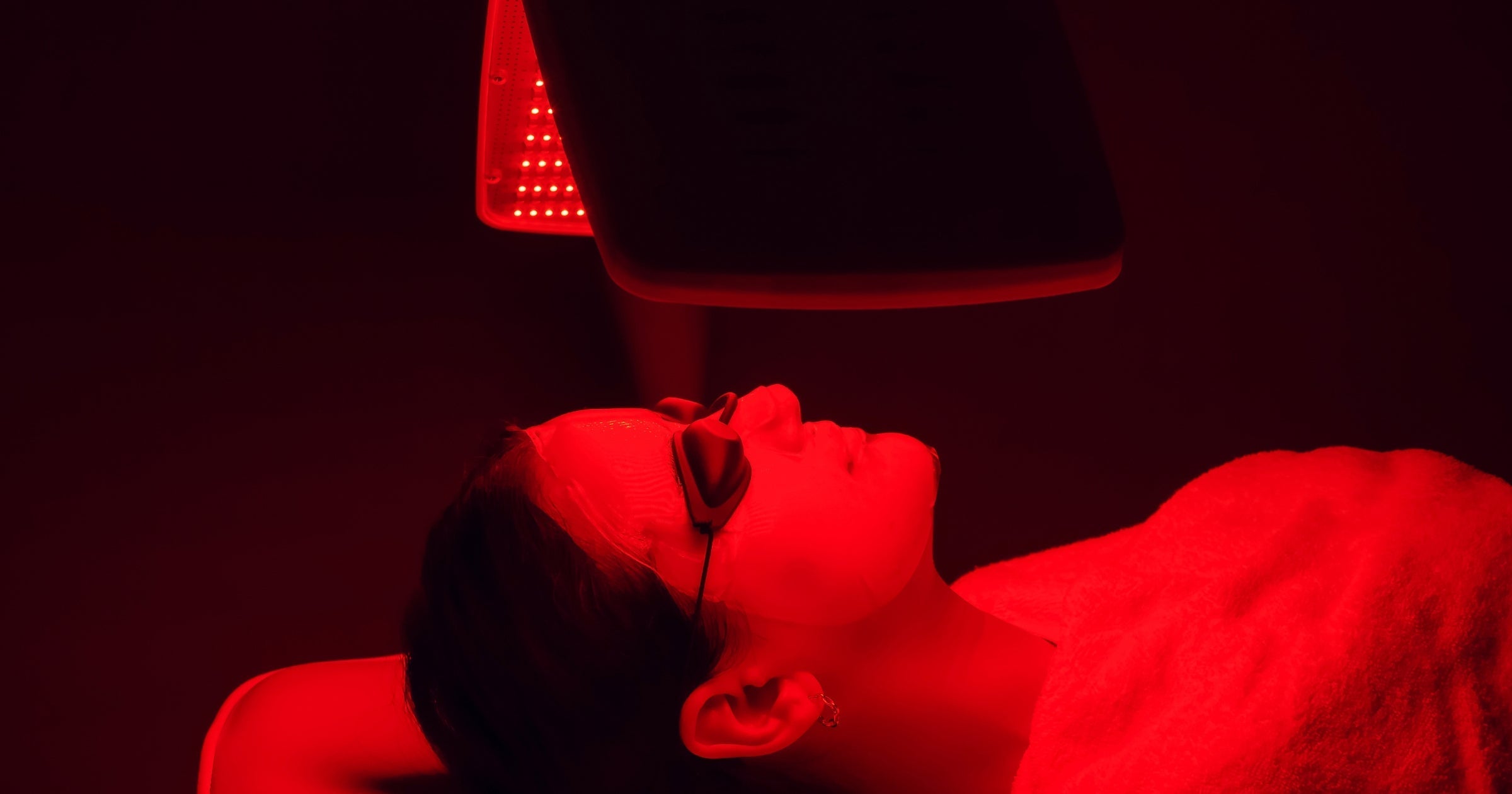 Woman receiving red light therapy facial treatment, wearing protective goggles, in a spa setting.