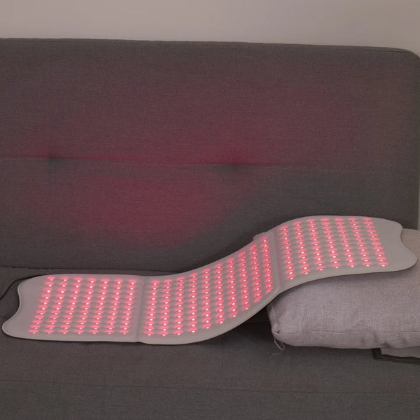 Flexible red light therapy pad with LED lights glowing, placed on a gray sofa